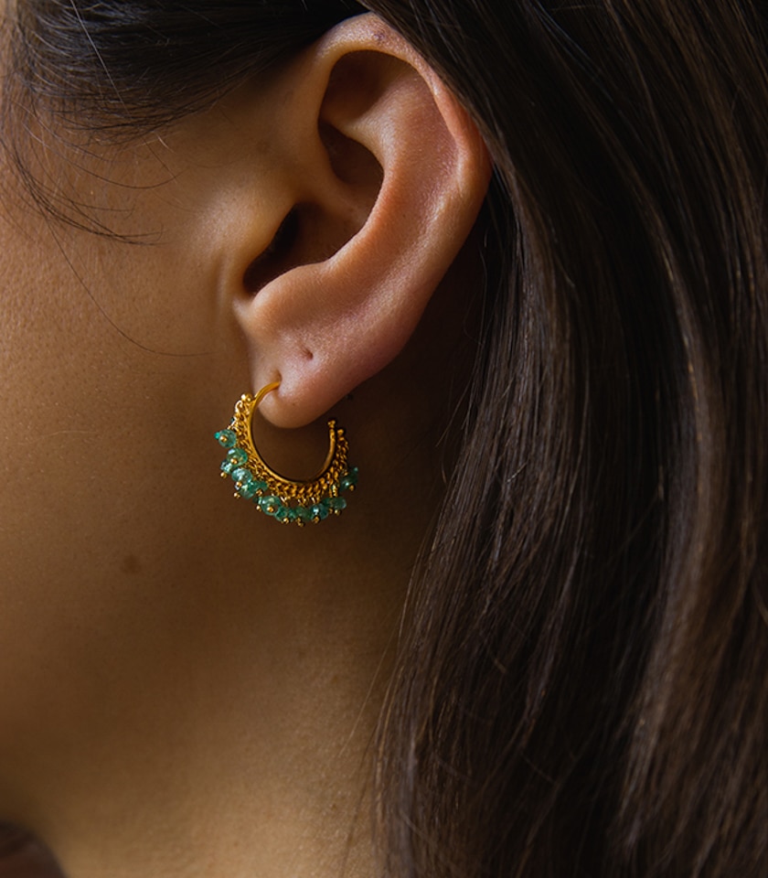 Close up of a model wearing emerald and gold hoop earrings