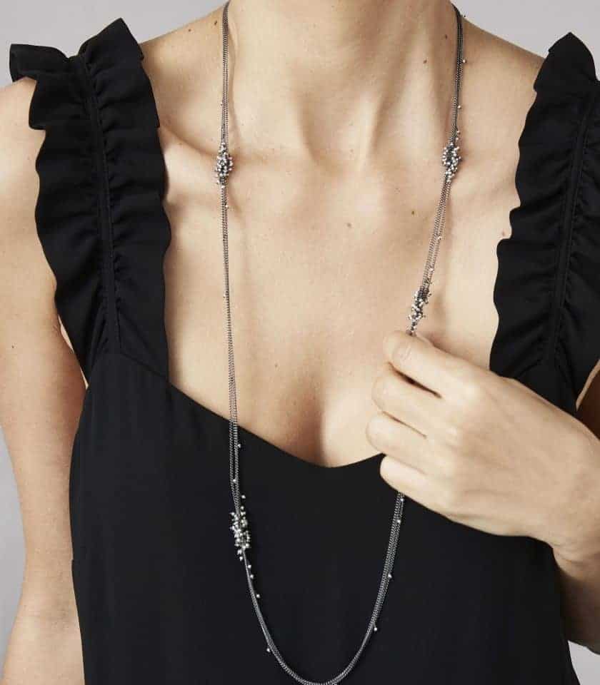 Photo of body of model wearing long necklace with several chains of oxidised silver and clusters of pearls.