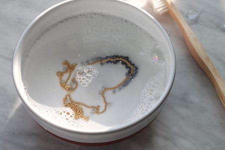 Photo of bowl of soapy water with beaded gold chain and cleaning brush.