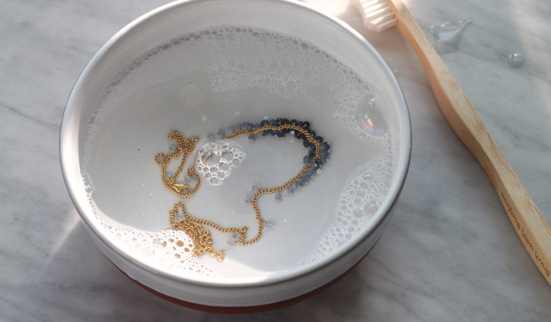Photo of bowl of soapy water with beaded gold chain and cleaning brush.