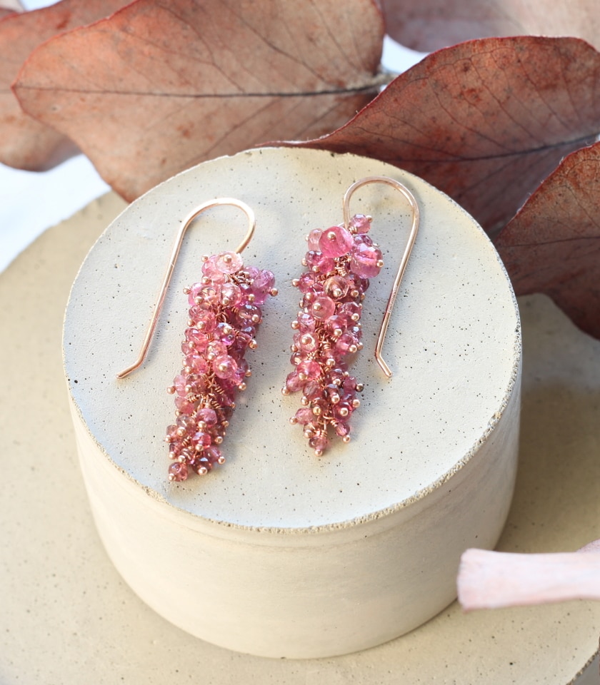 Photo of a pair of pink tourmaline beaded drop earrings on a block with leaves in the background