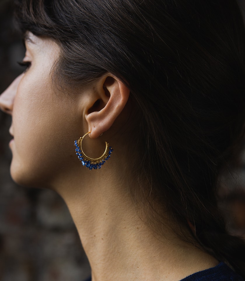 A dark haired model wearing a pair of blue sapphire beaded hoop earrings in gold vermeil