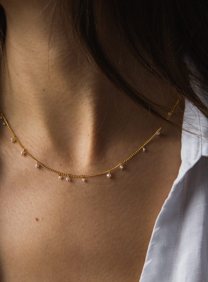 A close up of a model wearing a white shirt and a pearl and gold vermeil beaded necklace