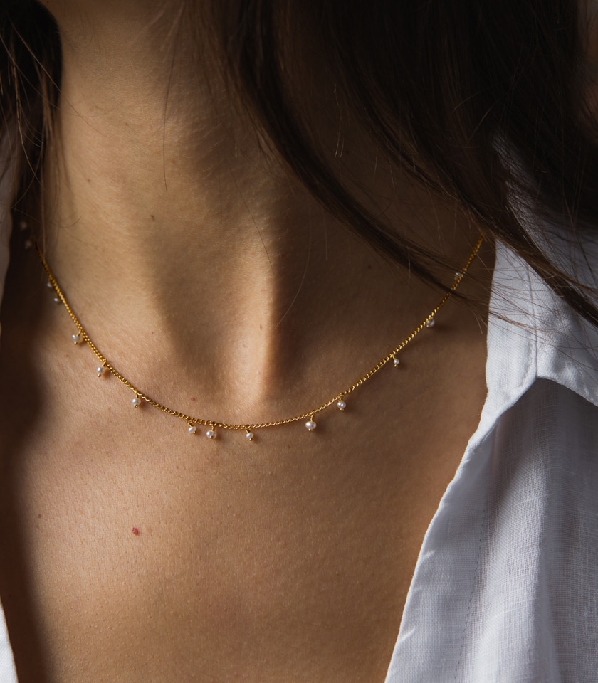 A close up of a model wearing a white shirt and a pearl and gold vermeil beaded necklace
