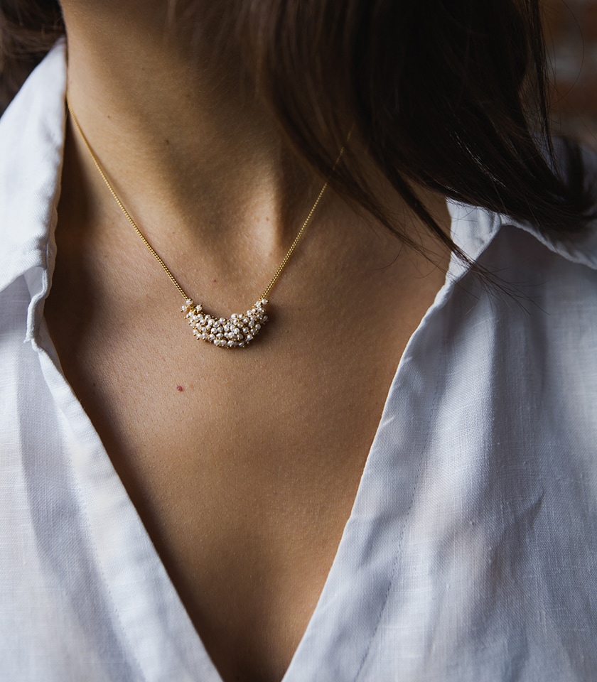 A model's neck and shoulders wearing a white shirt and a seed pearl and gold vermeil chain necklace