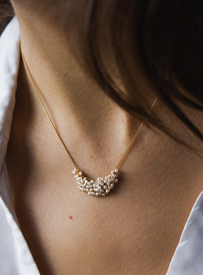A close up of a model wearing a white shirt and a pearl and gold plated silver cluster necklace