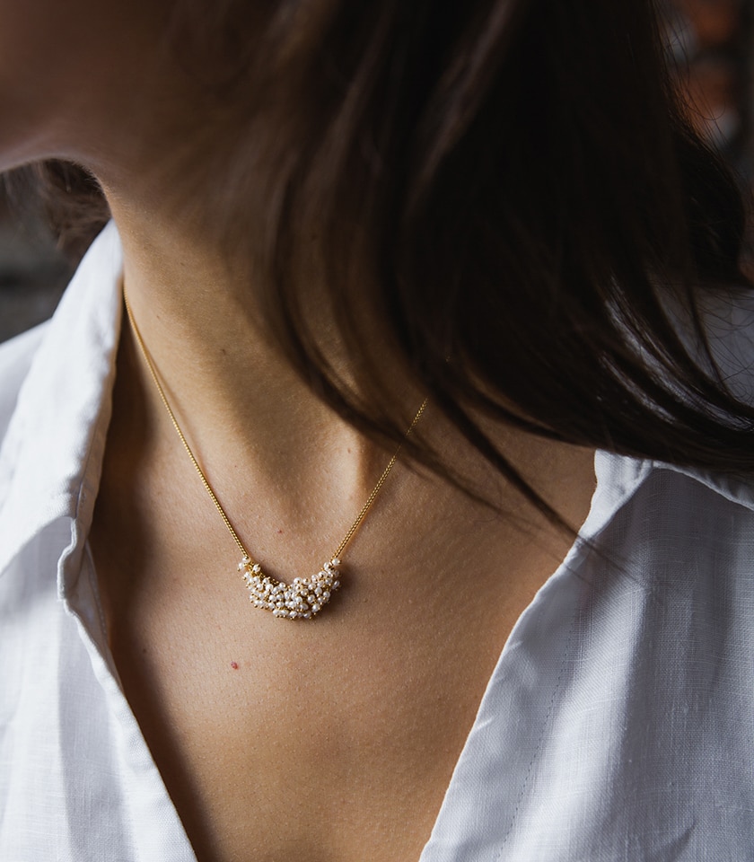 A model's neck and shoulders wearing a white shirt and a seed pearl and gold plated silver chain necklace