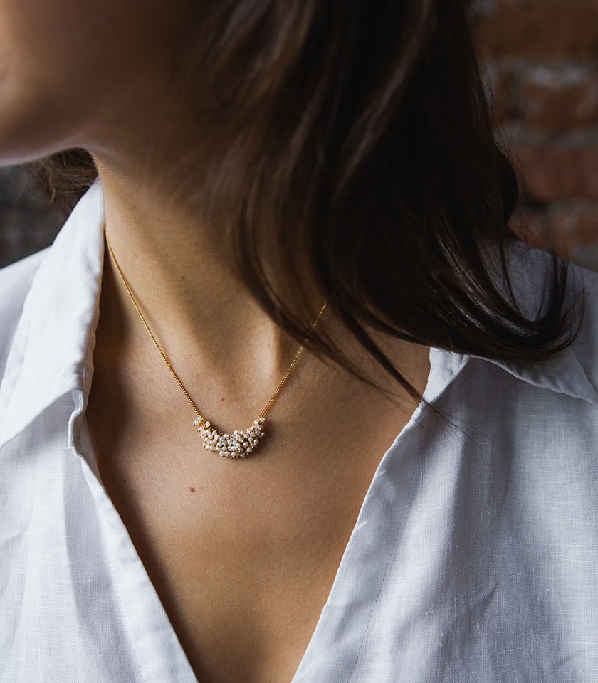 A model's shoulders wearing a white shirt and a seed pearl and gold plated silver chain necklace