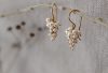 A pair of grape shaped pearl and gold vermeil earrings on a twig in front of a grey linen backdrop