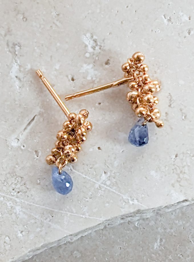 Sapphire teardop stud earrings in gold vermeil on a stone background.