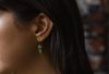 Green emerald drop earrings worn by a dark haired model