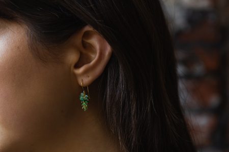 Green emerald drop earrings worn by a dark haired model